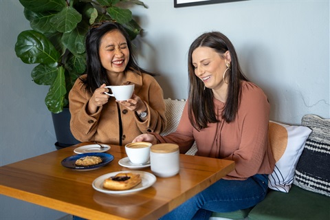 Two ladies enjoying a coffee in a cafe while laughing